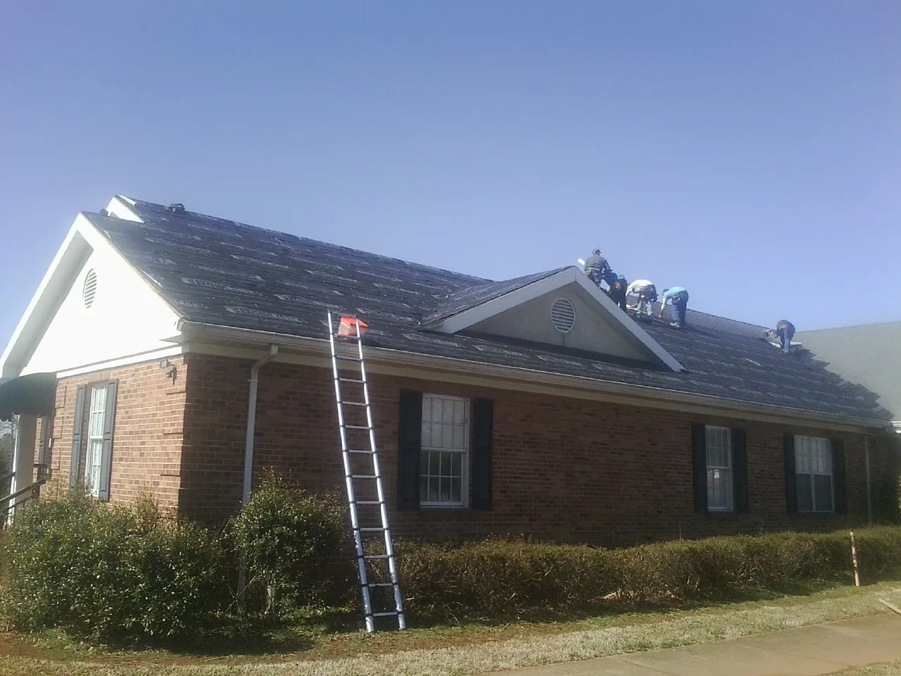 Crew tearing shingles off a brick ranch roof with a ladder set — Emergency Roof Repair work by our crew in West Newton