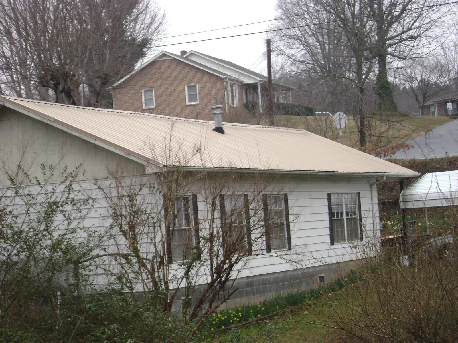 Tan metal roof on a white sided house set into a hillside — Commercial Roofing by Roofing Brothers in West Newton
